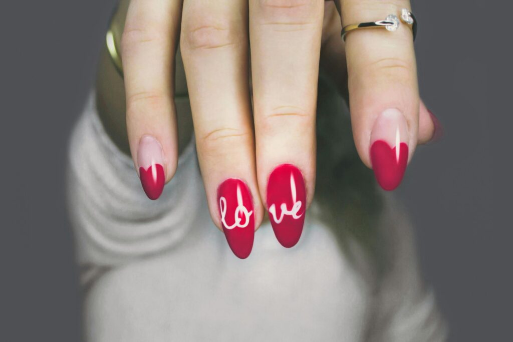 Vibrant red nails with 'love' art on a woman's hand, showcasing elegant style and design.|Nailcarewithsam