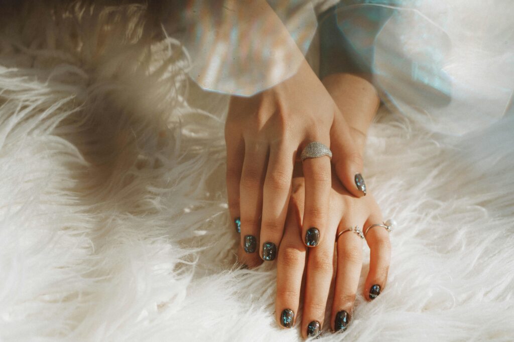 Close-up of a woman's hands wearing rings and nail art, resting on white faux |nailcarewithsam